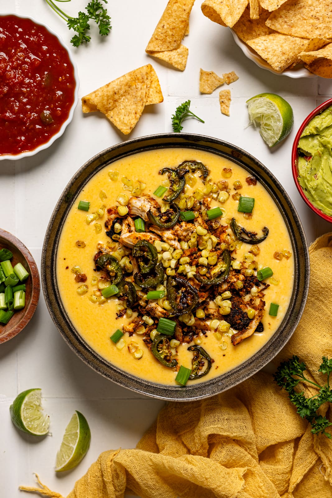 Queso dip on a white tile table with tortilla chips and salsa.