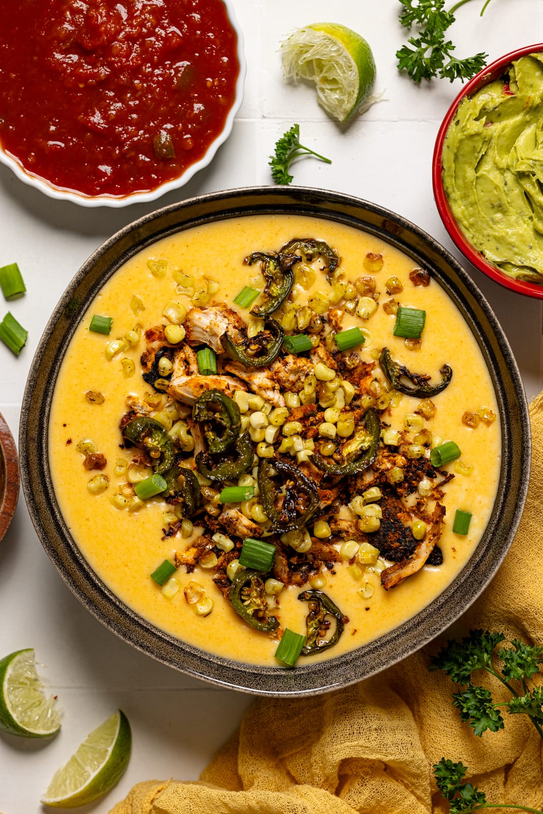 Queso dip with toppings and salsa, guacamole, and lime wedges.