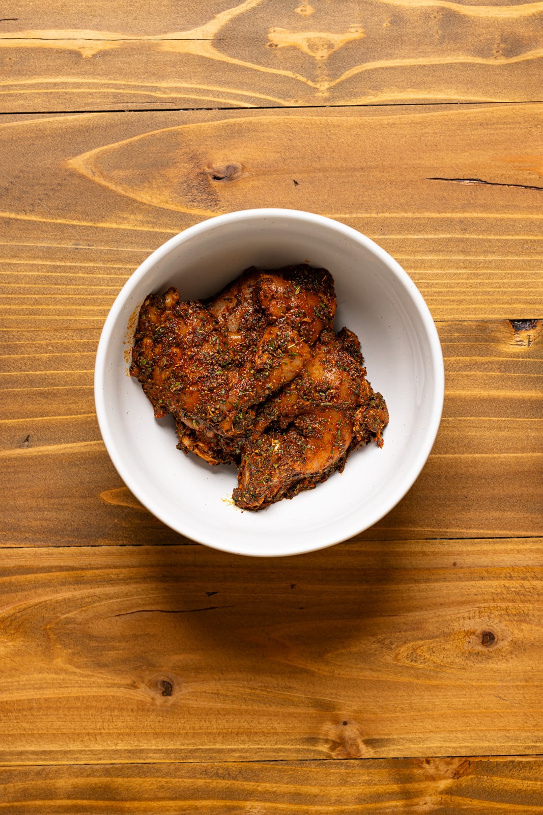 Seasoned + marinated chicken in a white bowl.