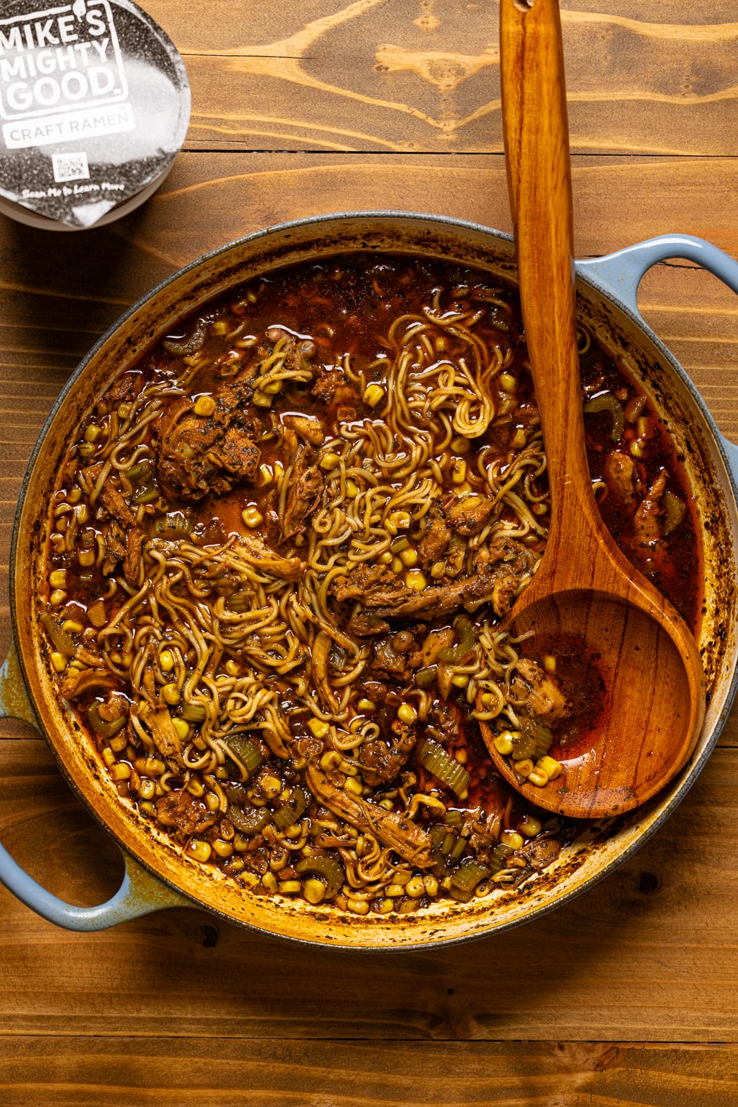 Cooked chicken and ramen in a dutch oven and a wooden spoon.