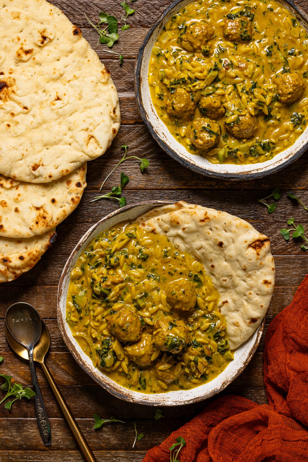 Two bowls of soup with naan bread and two spoons.