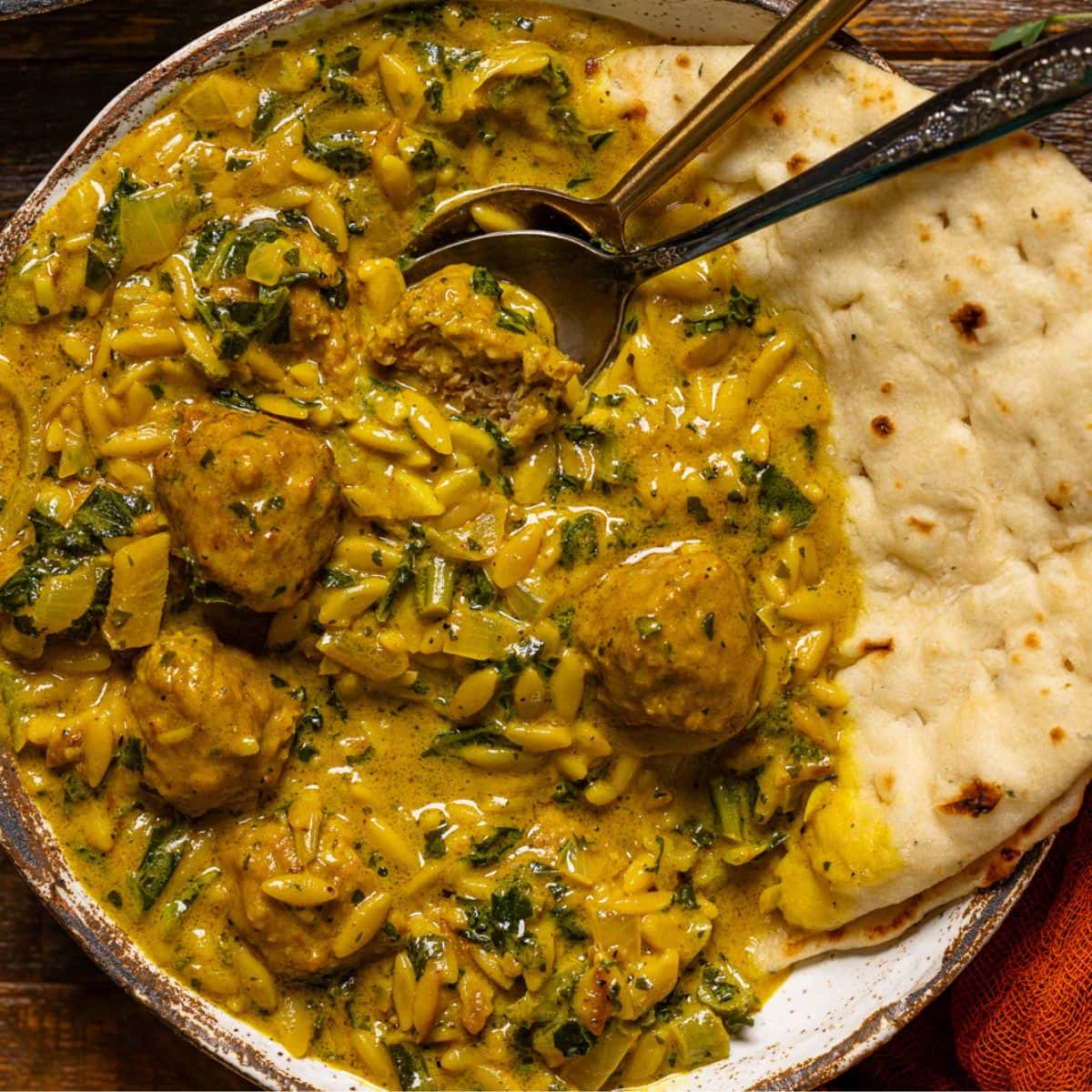 Up close shot of curry soup with naan bread and two spoons.