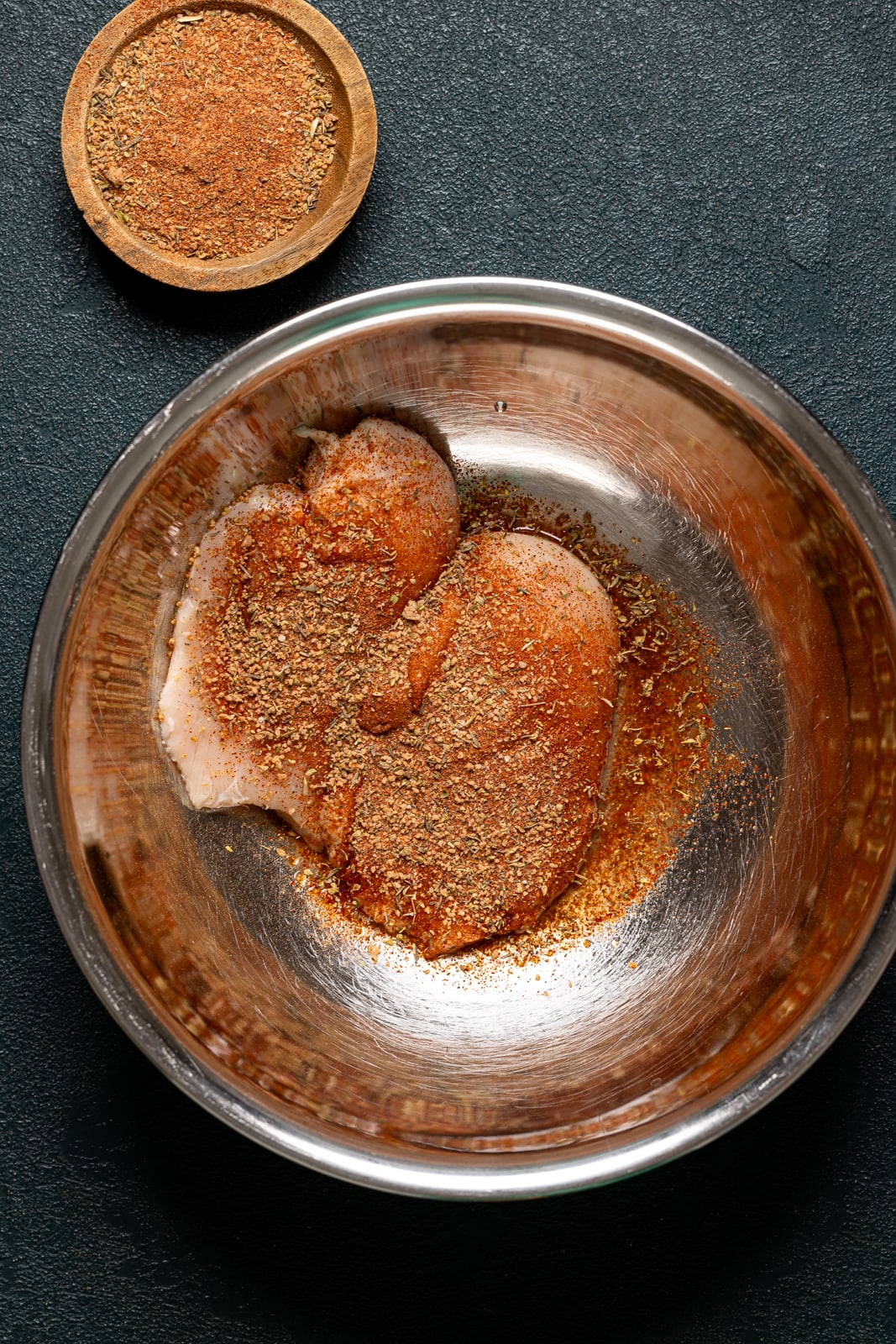 Chicken breasts in a bowl with seasoning. 