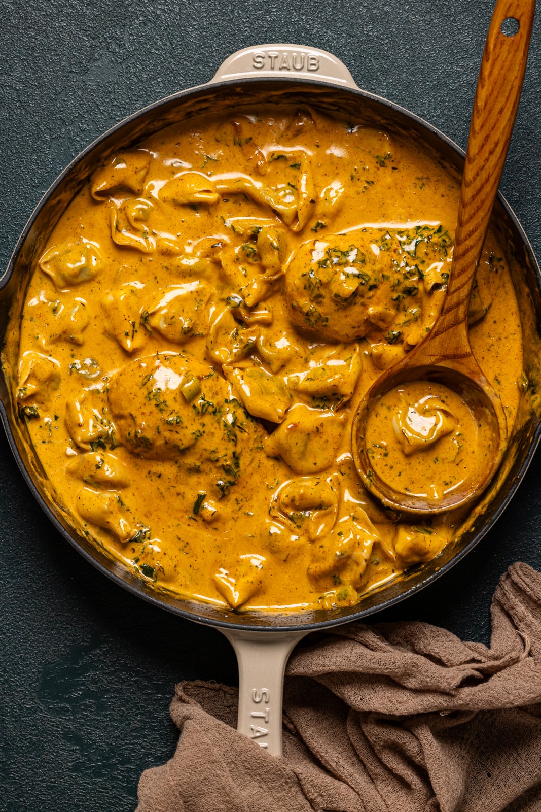 Creamy chicken and tortellini in a skillet with a wooden spoon.