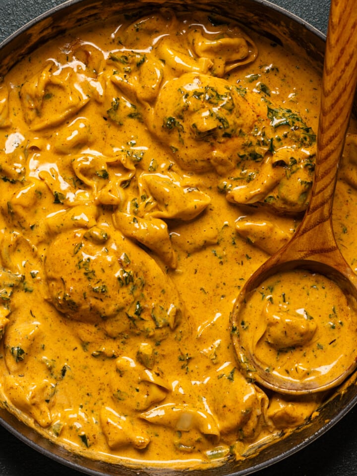 Up close of creamy chicken and tortellini in a skillet with a wooden spoon.