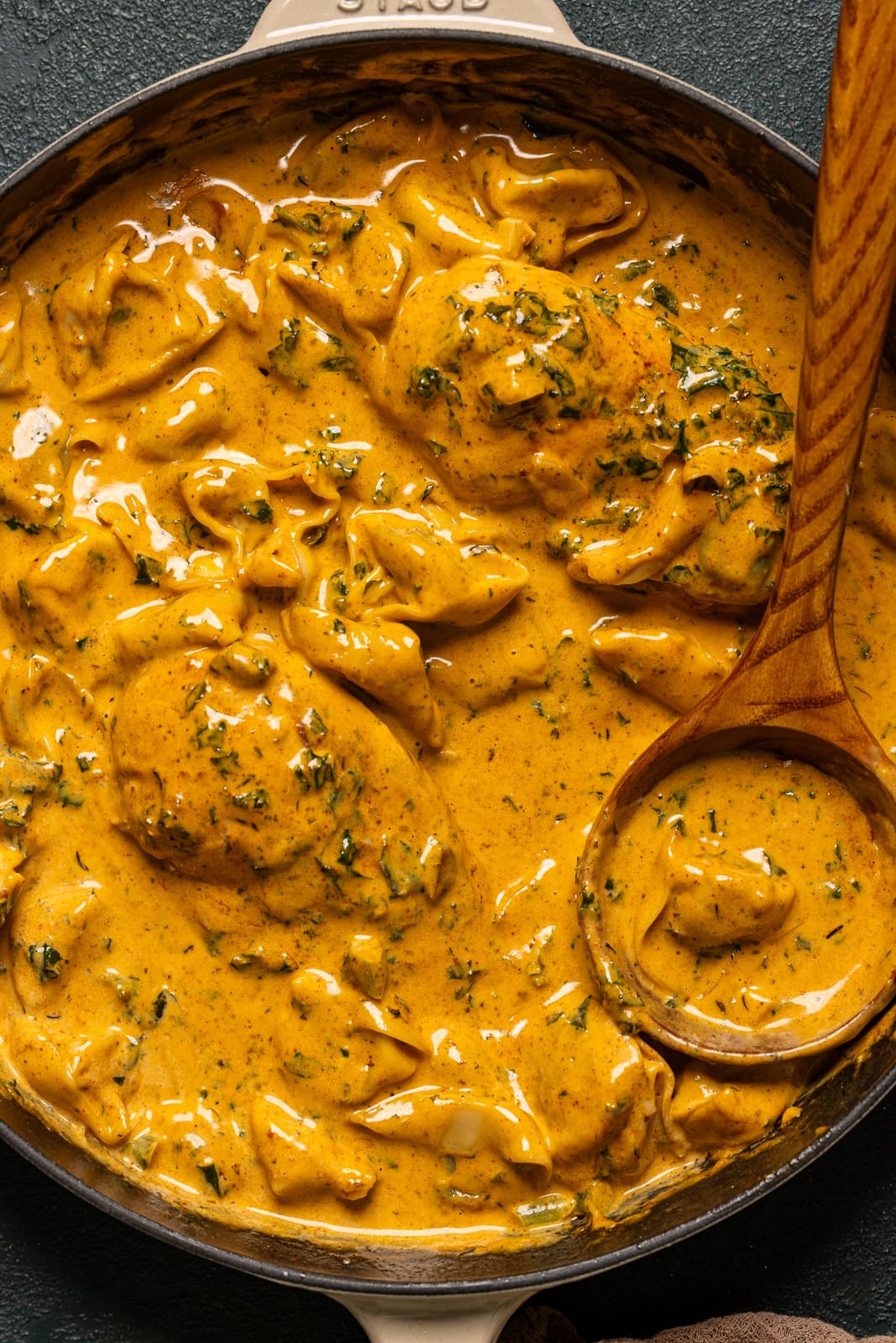 Up close of creamy chicken and tortellini in a skillet with a wooden spoon.