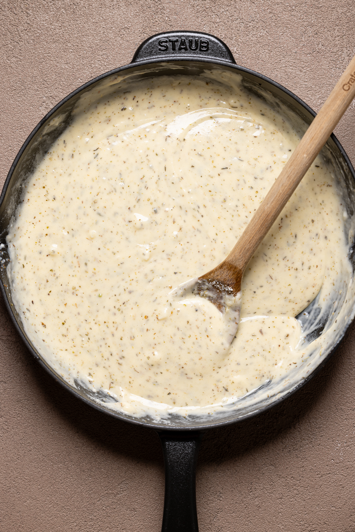 Image of garlic parmesan sauce in a black skillet with wooden spoon.