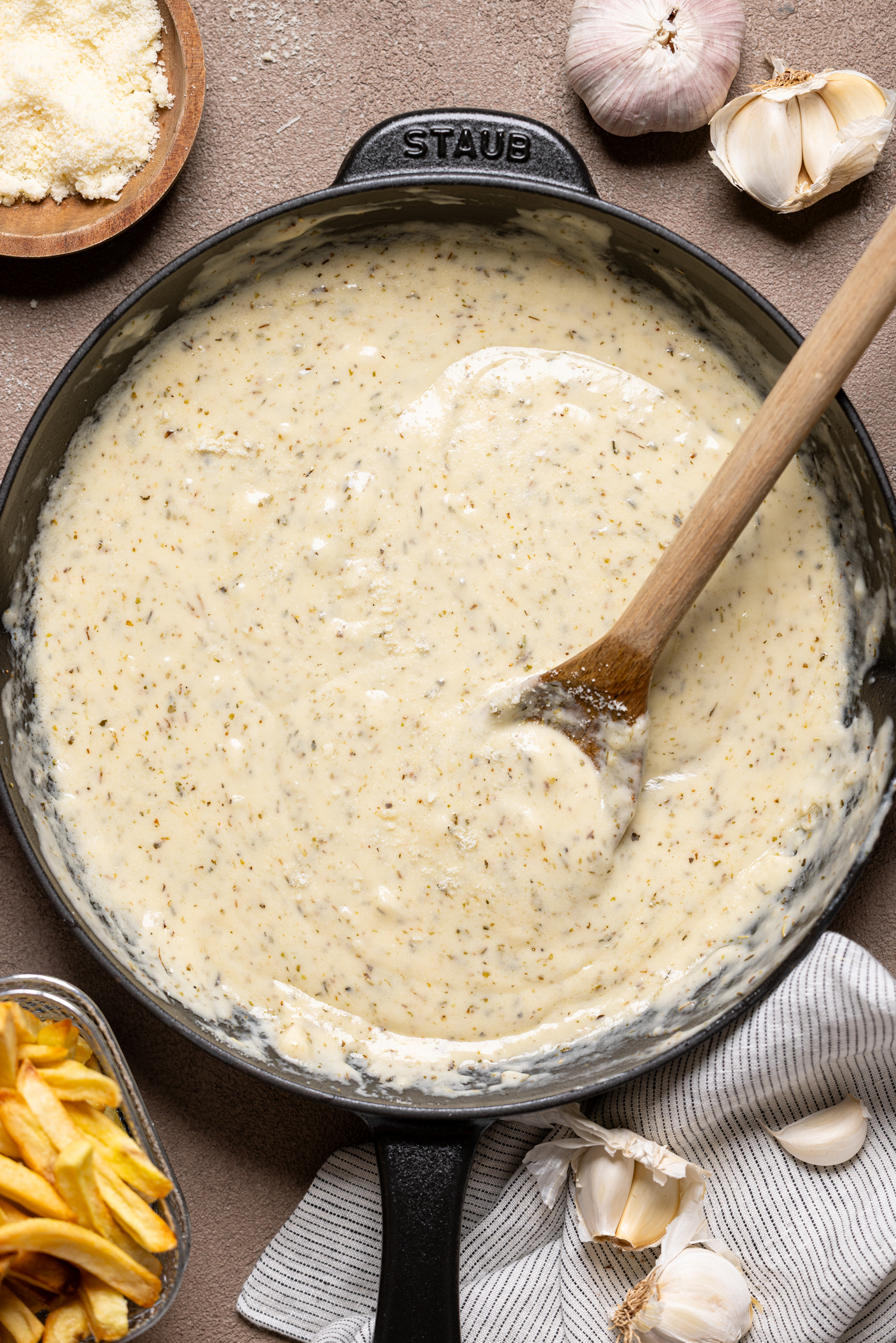 Image of sauce in a black skillet with wooden spoon and garlic cloves.