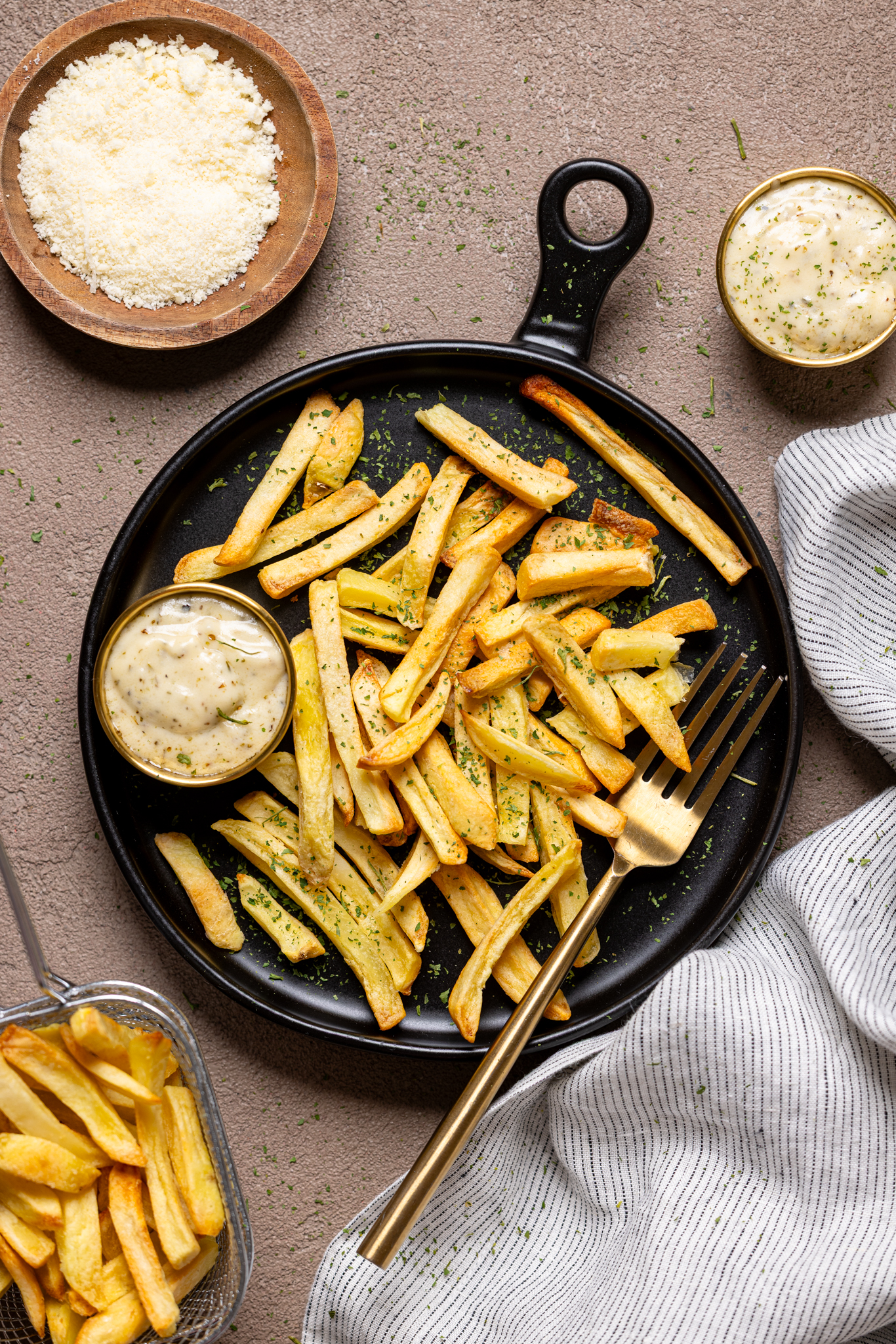 Image of garlic parmesan sauce in dipping bowls with fries on a black plate with forks.