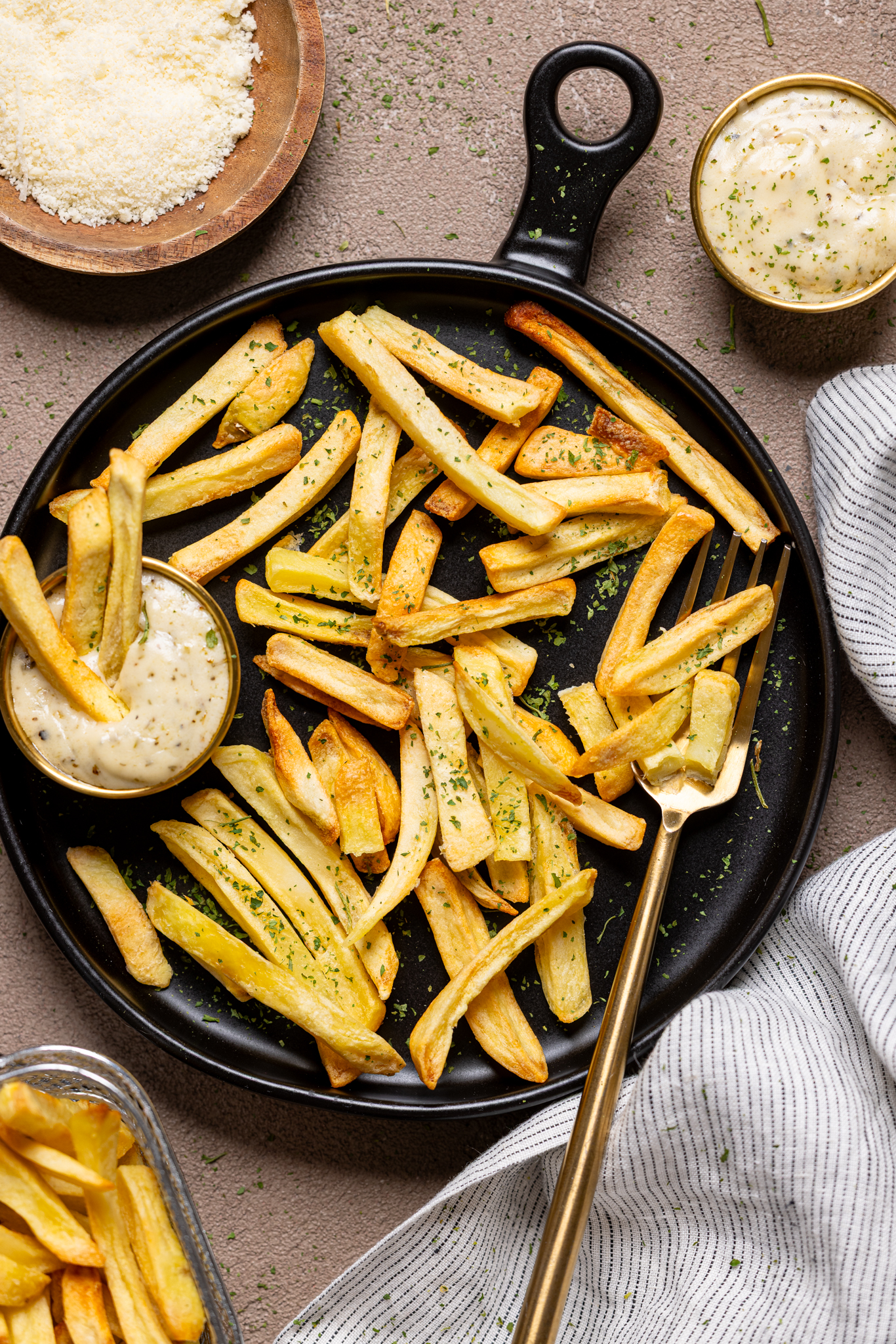 An image of french fries on a black plate with parmesan garlic dipping sauce. 