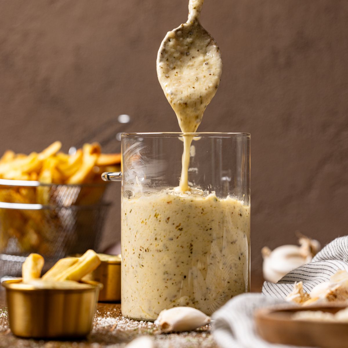 Image of garlic parmesan sauce in a jar with a spoon held with sauce.