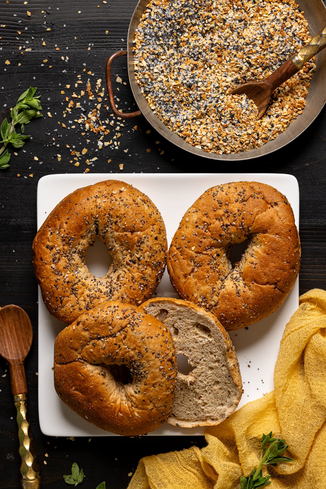 Everything bagels + seasoning on a black wood table.