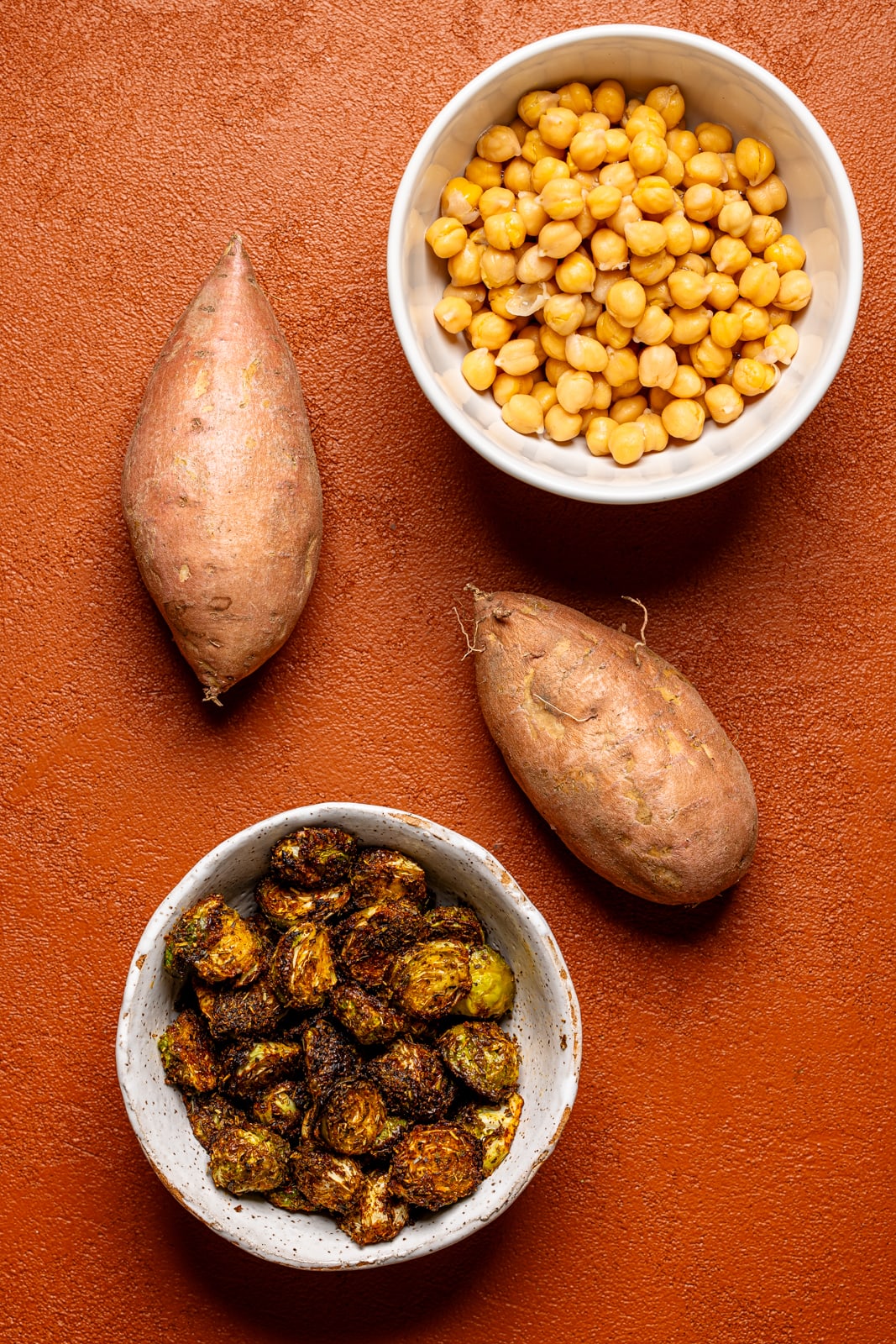 Sweet potato, chickpeas, and Brussels Sprouts on a burnt orange table.