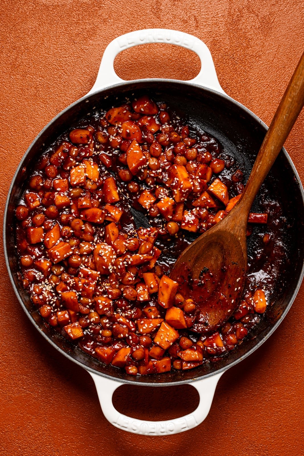 Gochujang sweet potatoes and chickpeas in a skillet with a wooden spoon.