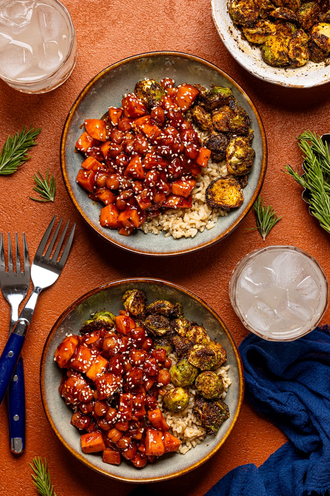 Two bowls of Gochujang food bowl with a drink, two forks, and a blue napkin. 