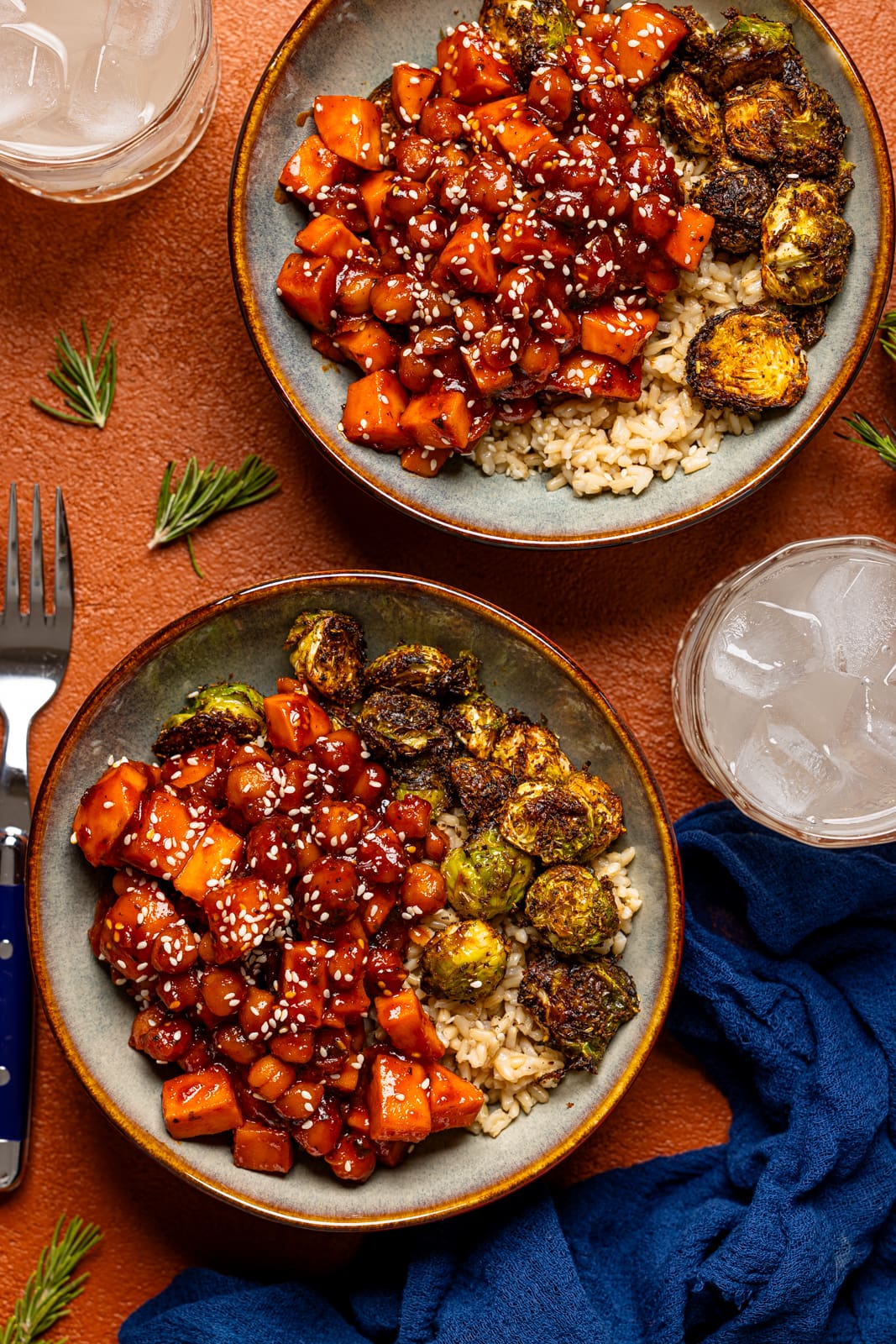 Two bowls of Gochujang sweet potatoes and chickpeas with two drinks and a fork.