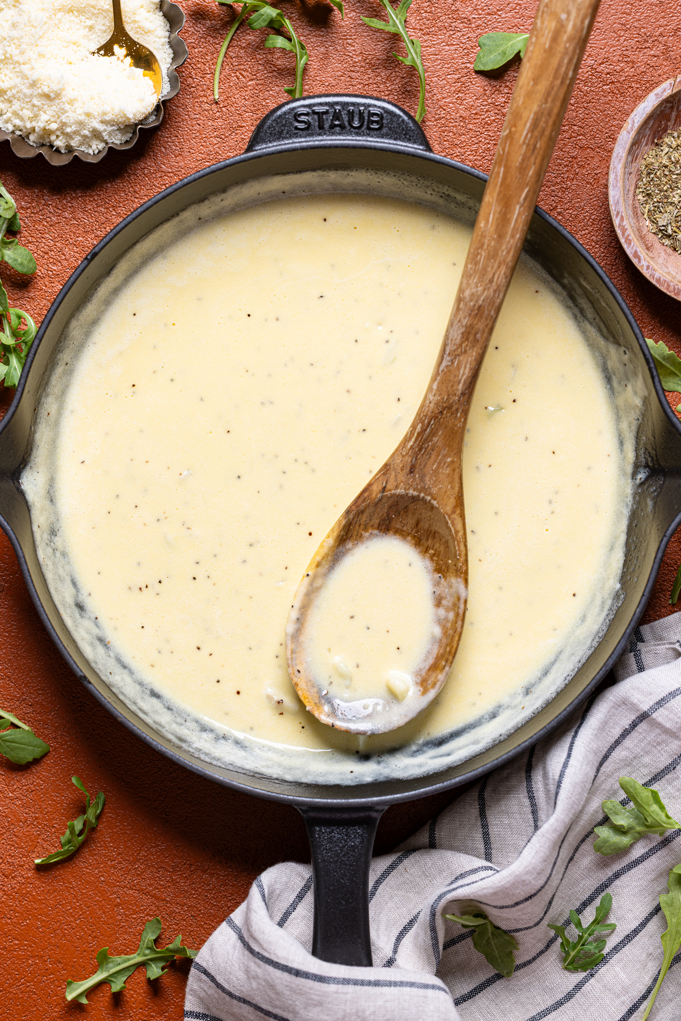 An image of alfredo sauce in a skillet with a wooden spoon and parmesan.
