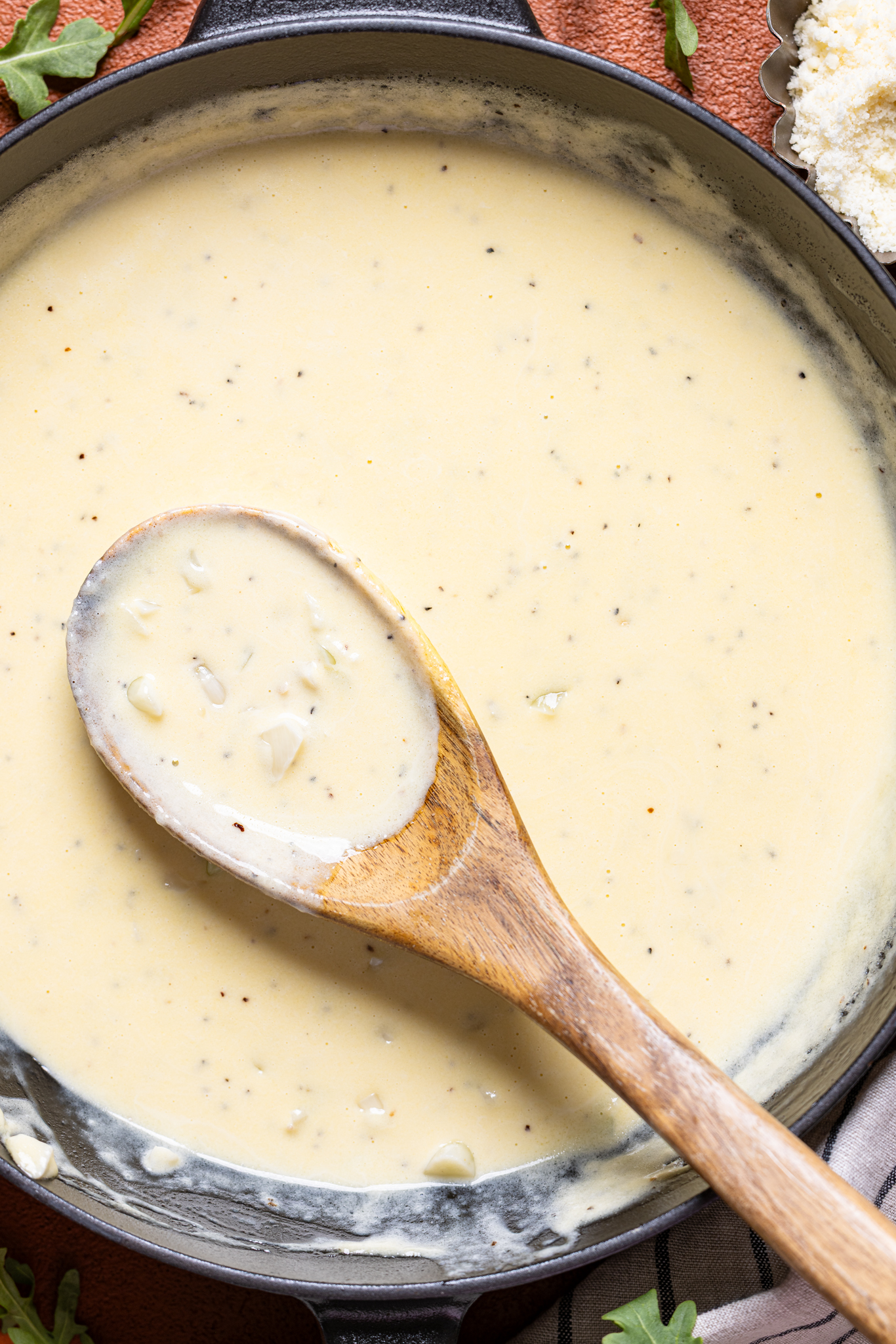 An image of alfredo sauce in a skillet with a wooden spoon.