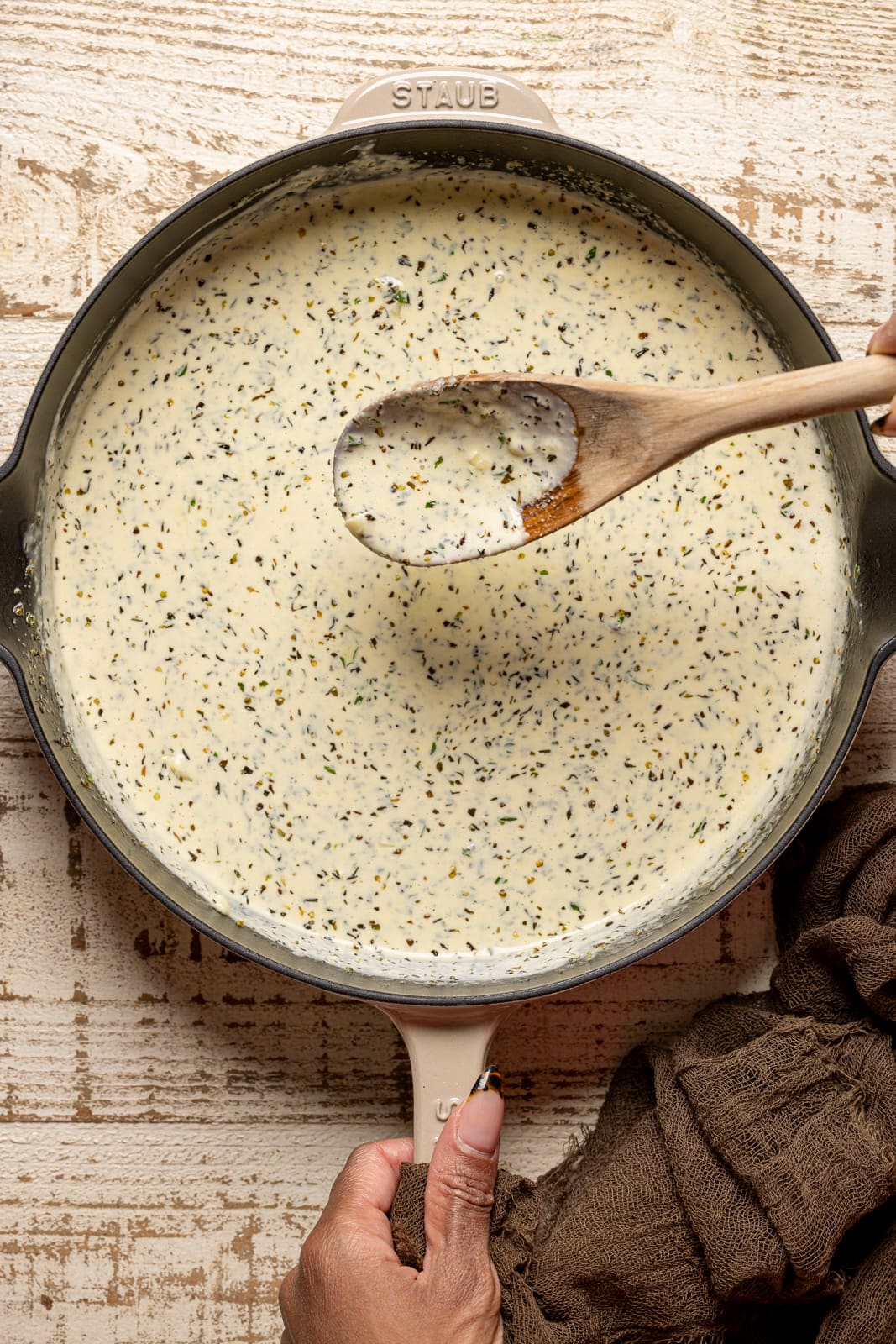 Alfredo sauce in a skillet being held with a wooden spoon.