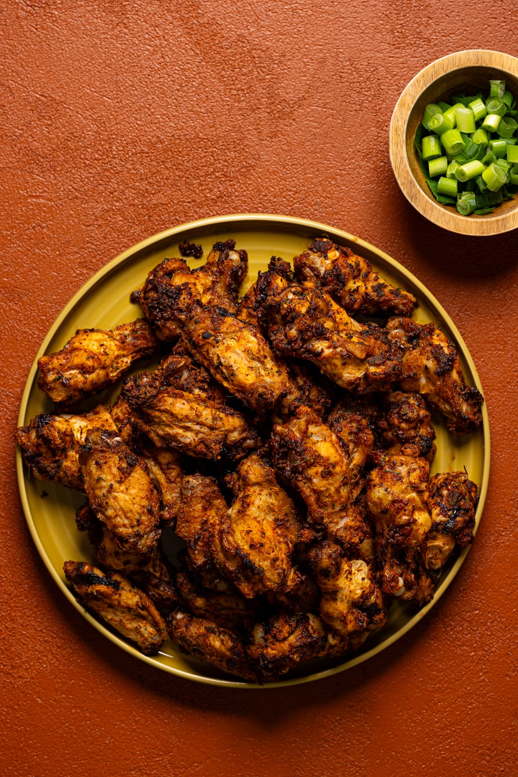 Chicken wings on a circular platter with a side of scallions. 