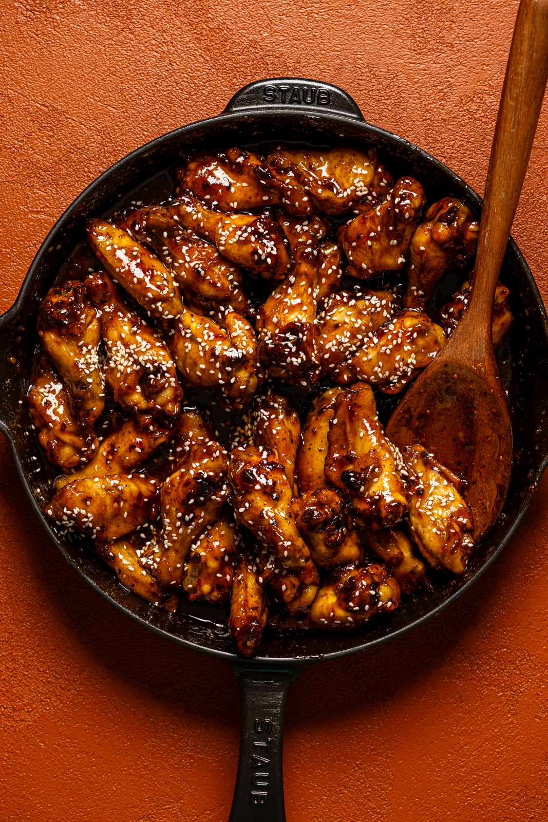 Chicken wings in a black skillet with a wooden spoon.