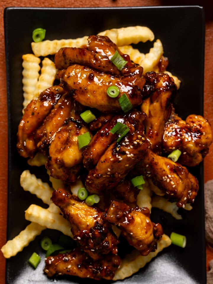 Wings served on top of fries on a black platter.