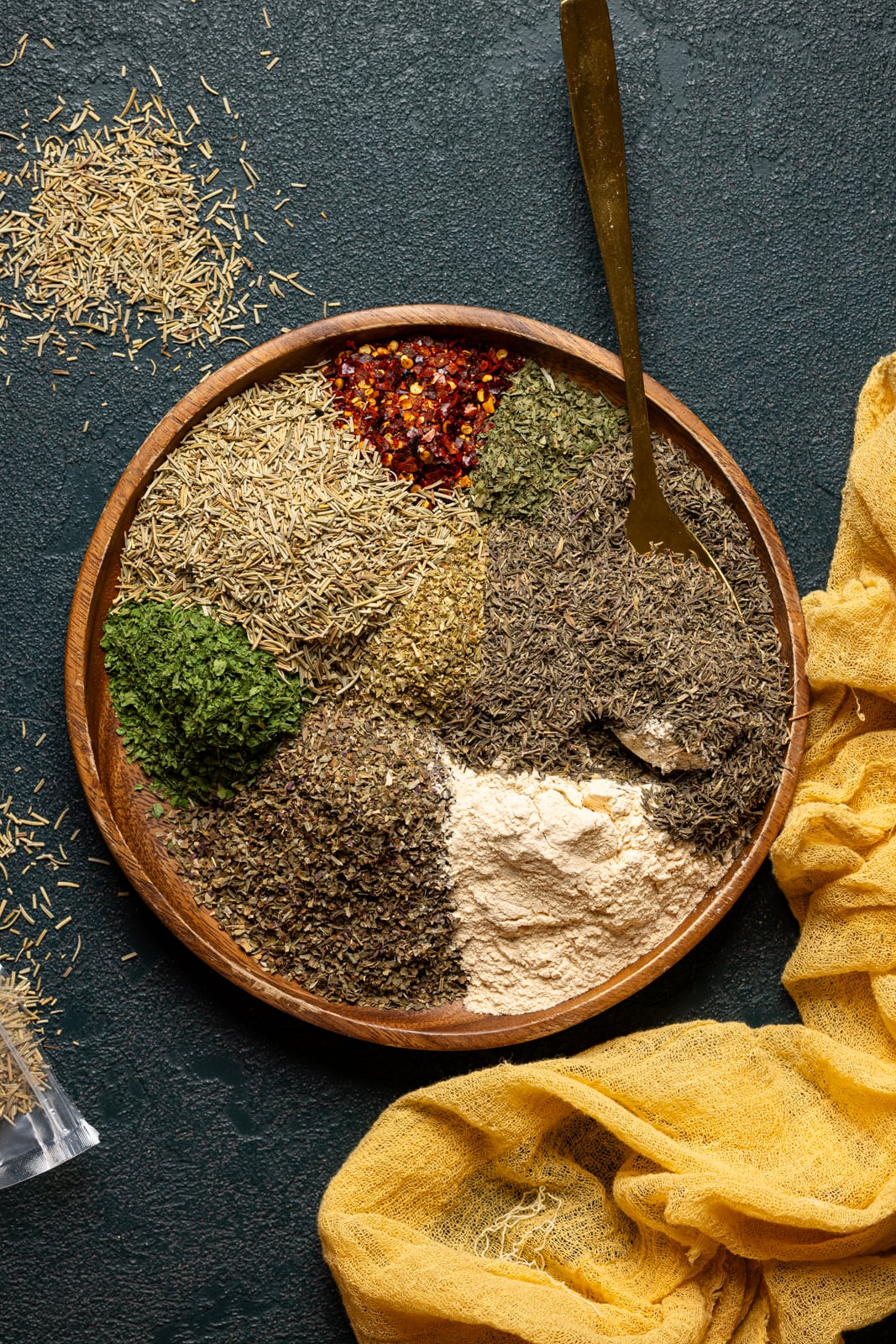 All seasonings together on a brown wood plate with a spoon.