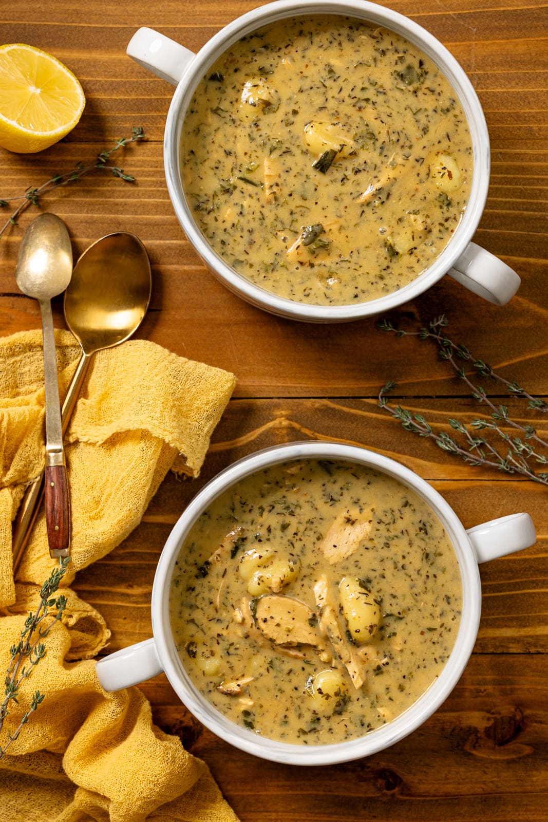Two bowls of creamy chicken soup with spoons and lemons.