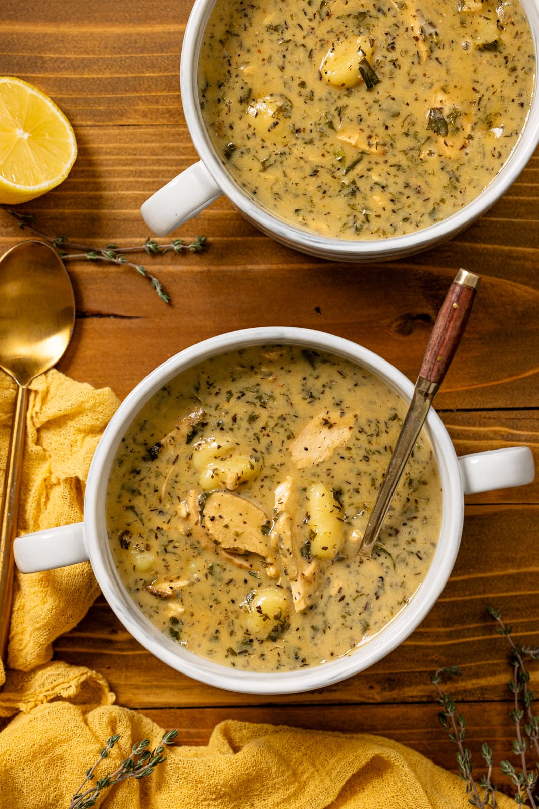 Bowls of creamy chicken soup with spoons and lemon wedges.