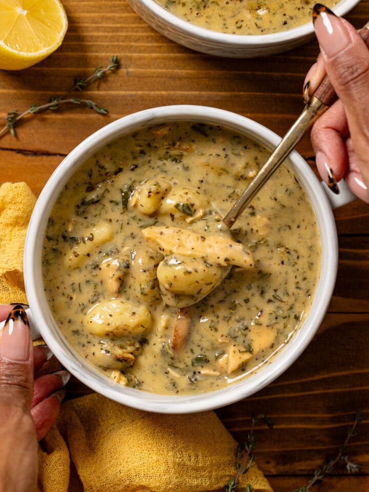 Bowl of soup in a white bowl being held with a spoon.