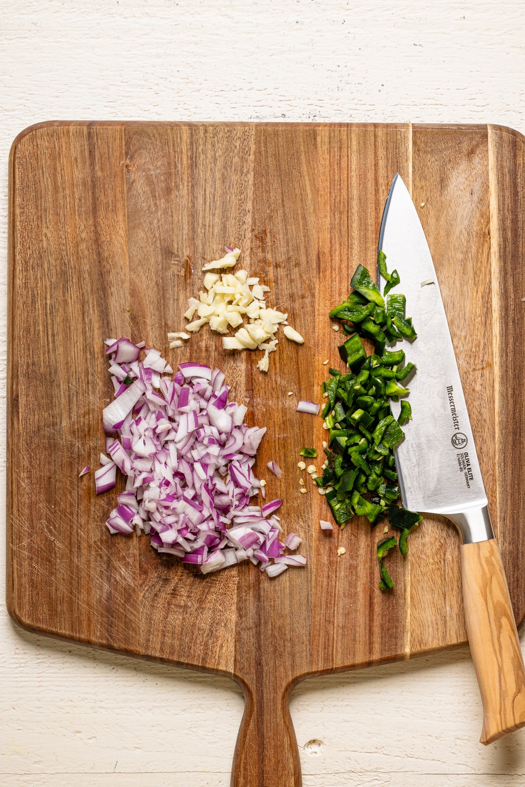 Chopped onions, garlic, and green onions on a cutting board with a knife.