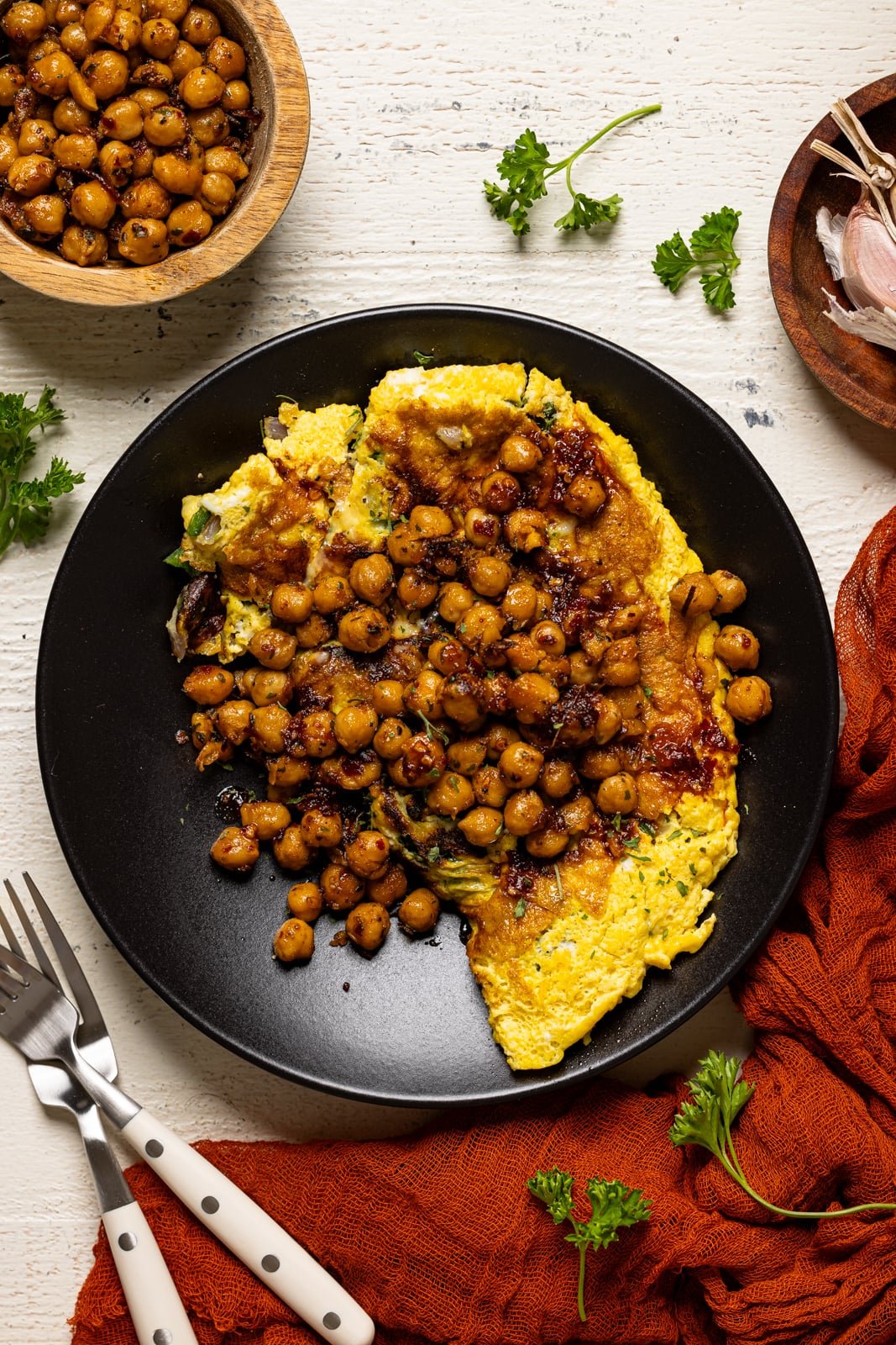 Omelette in a black plate with two forks and a side of chickpeas.