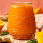 Up close shot of juice in a mason jar with oranges and ginger.