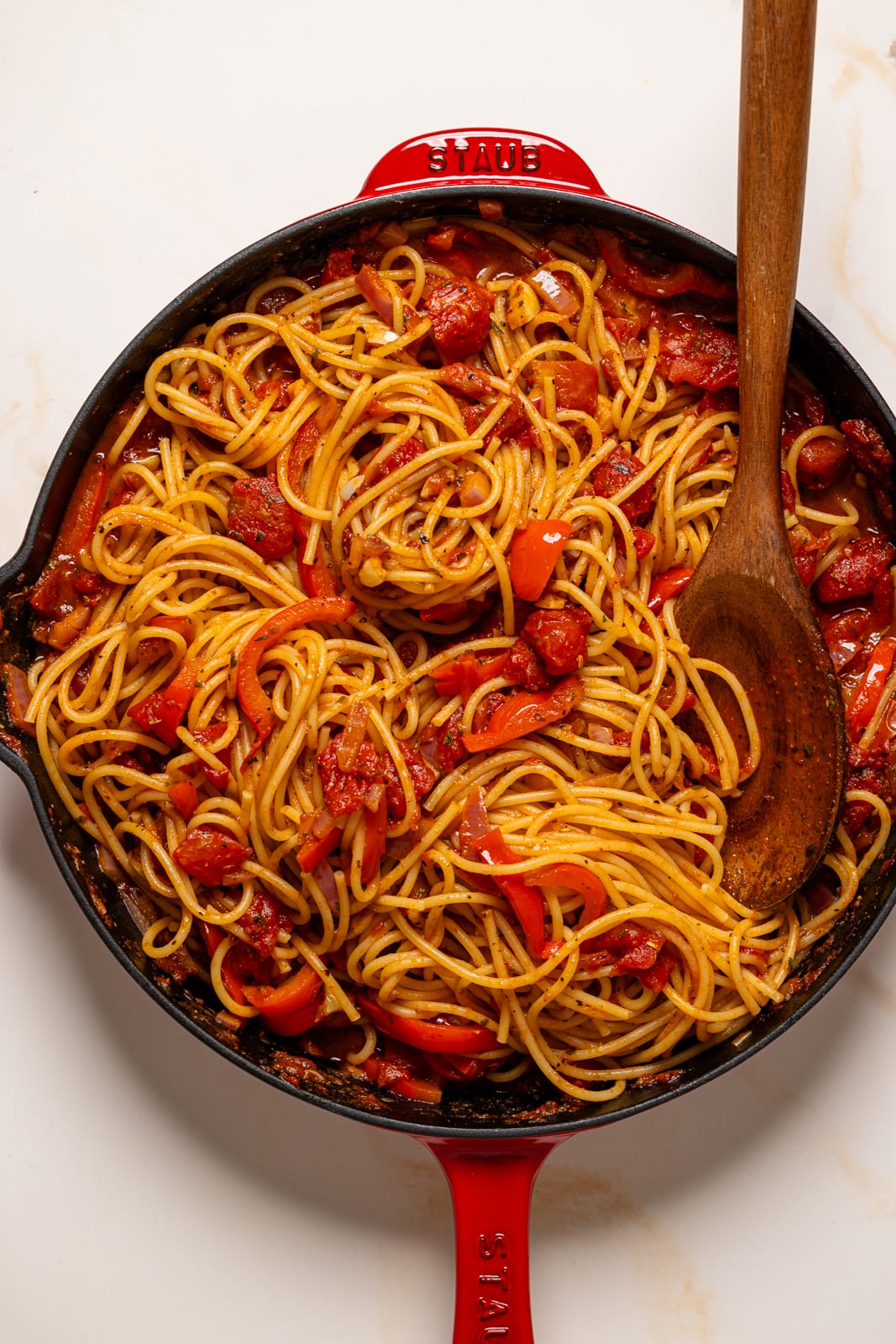 Cooked spaghetti in a red skillet with a brown wooden spoon.