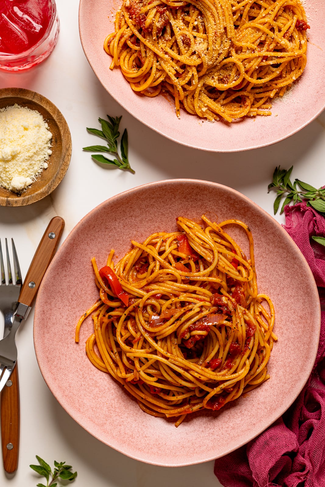 Two pink plates with spaghetti and two forks and a drink.