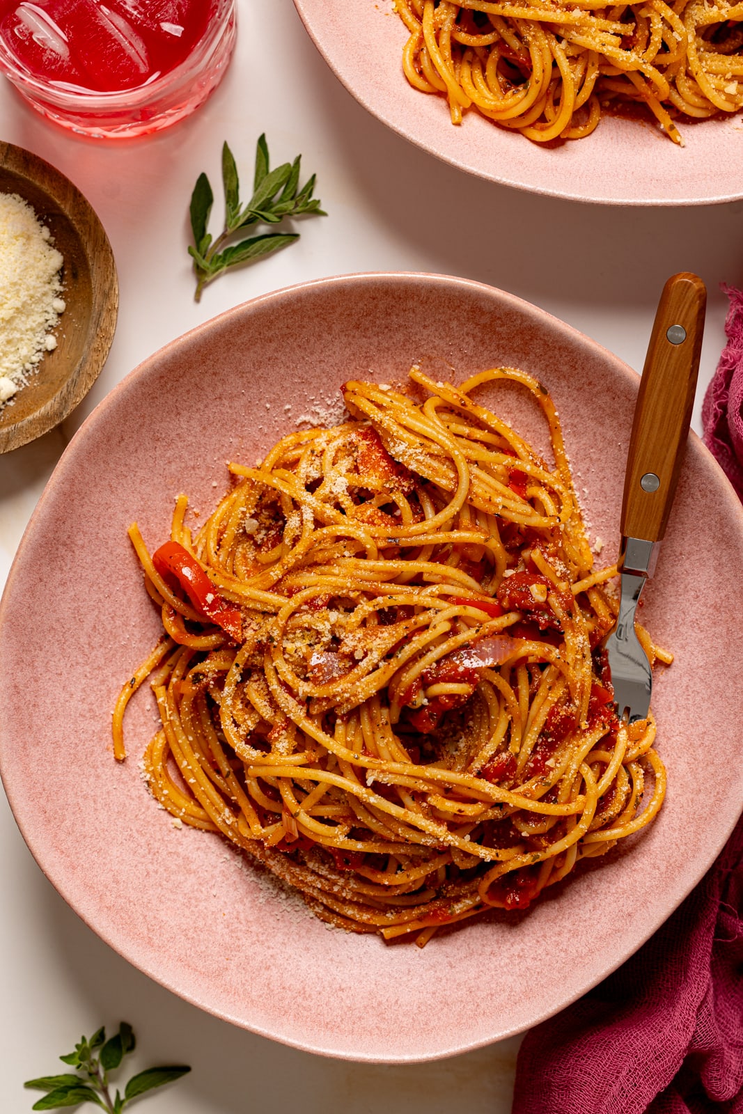 Spaghetti in two pink plates with a fork and parmesan cheese.