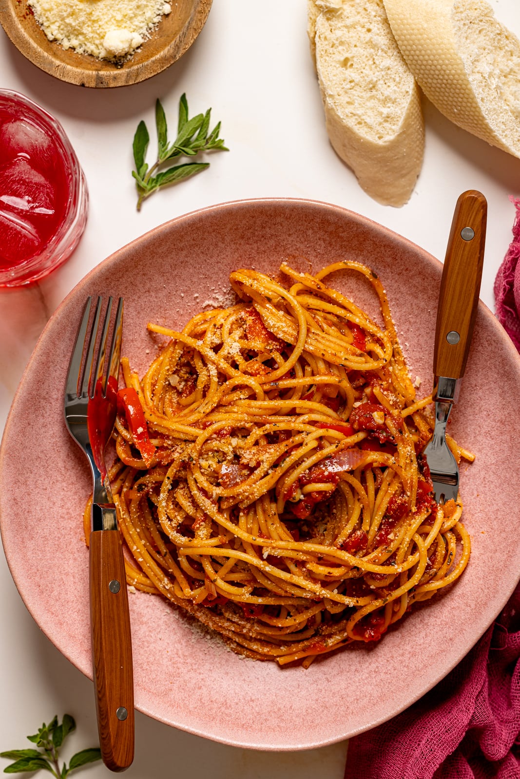 Spaghetti on a pink plate with two forks and a side of bread.