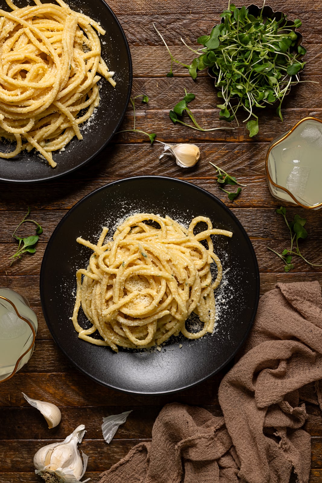 Two plates of pasta with drinks on a brown wood table.