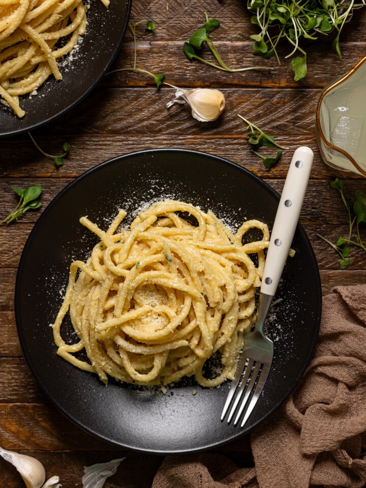 Two plates of pasta on a brown wood table with a fork.