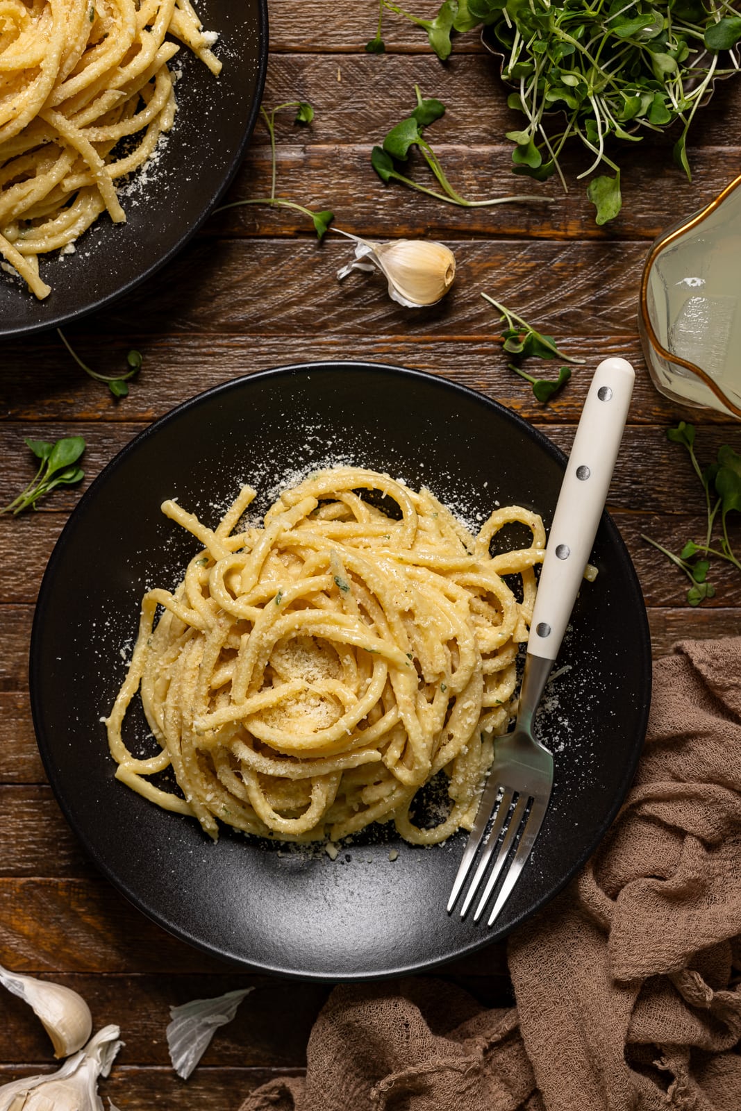 Two plates of pasta on a brown wood table with a fork.