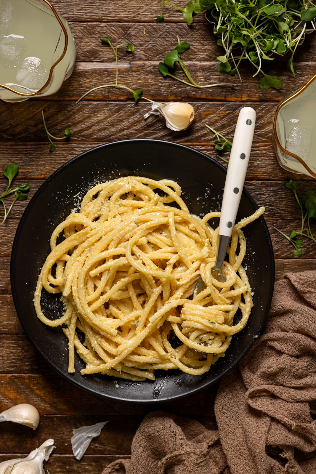 Up close shot of pasta in a black plate with a fork and two drinks.