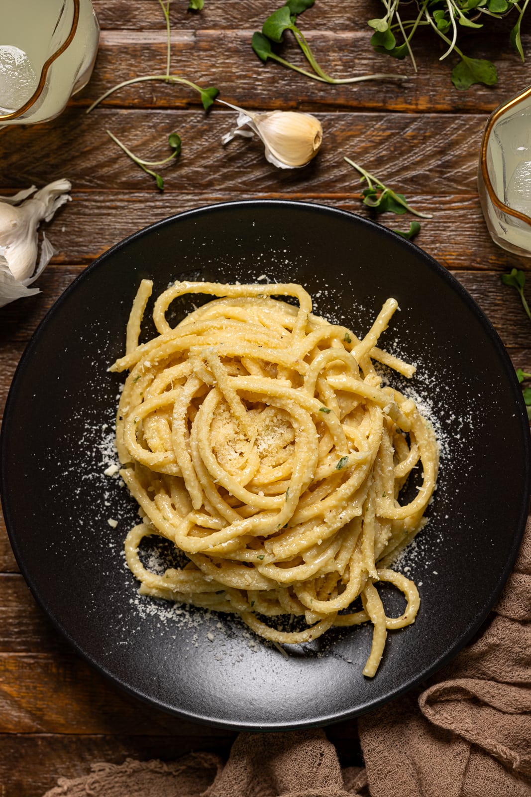 Pasta in a black plate on a brown wood table with drinks.