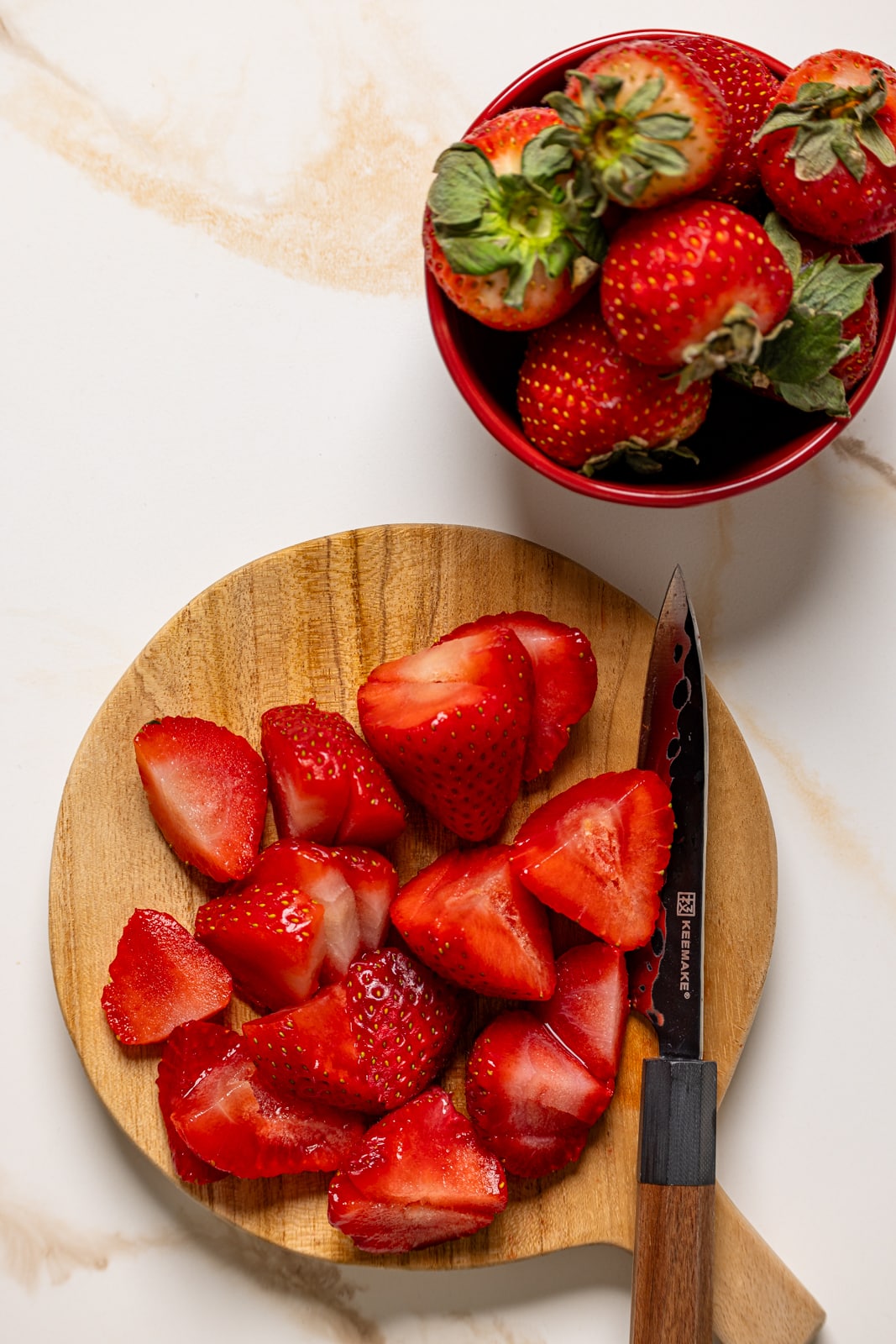 Cut fresh strawberries on a cutting board with a knife.