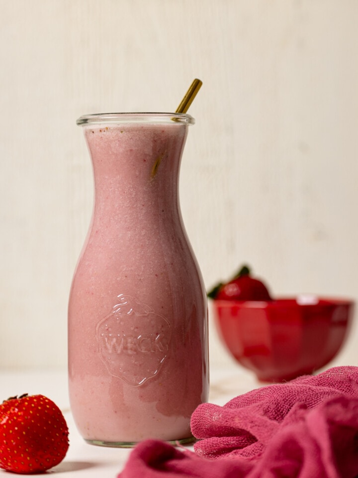 Strawberry milk in a jar with a straw and fresh strawberries.