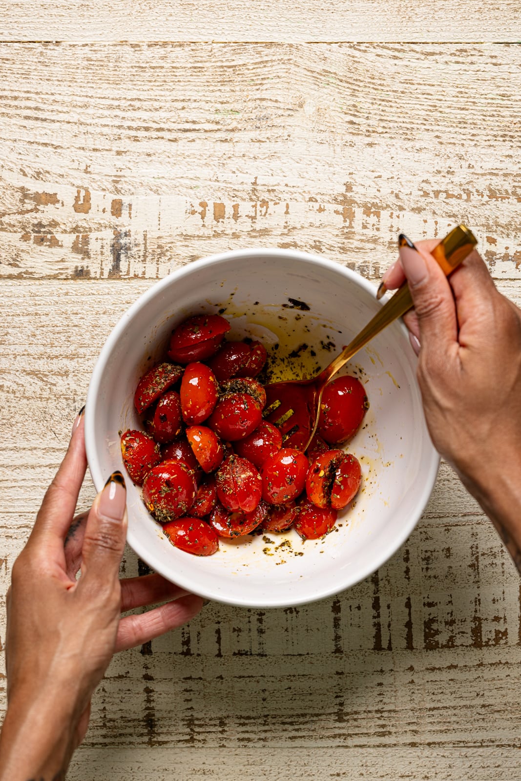 Bowl with tomatoes being mixed with a gold spoon.