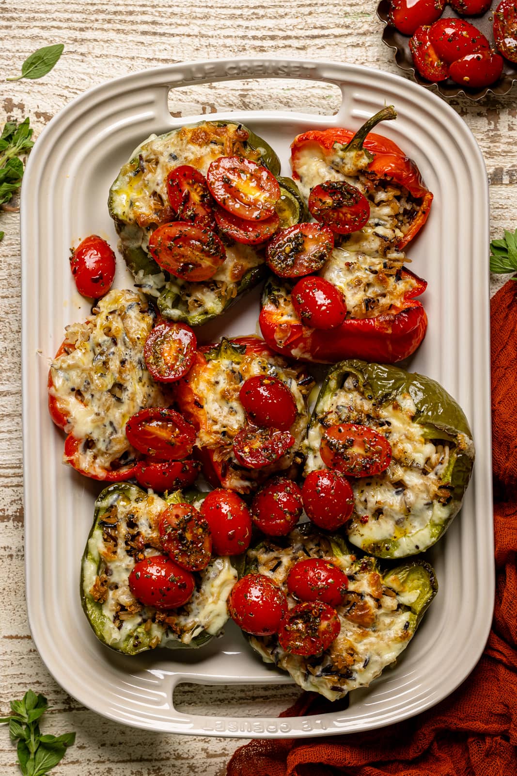 Stuffed peppers on a white serving platter with tomatoes.
