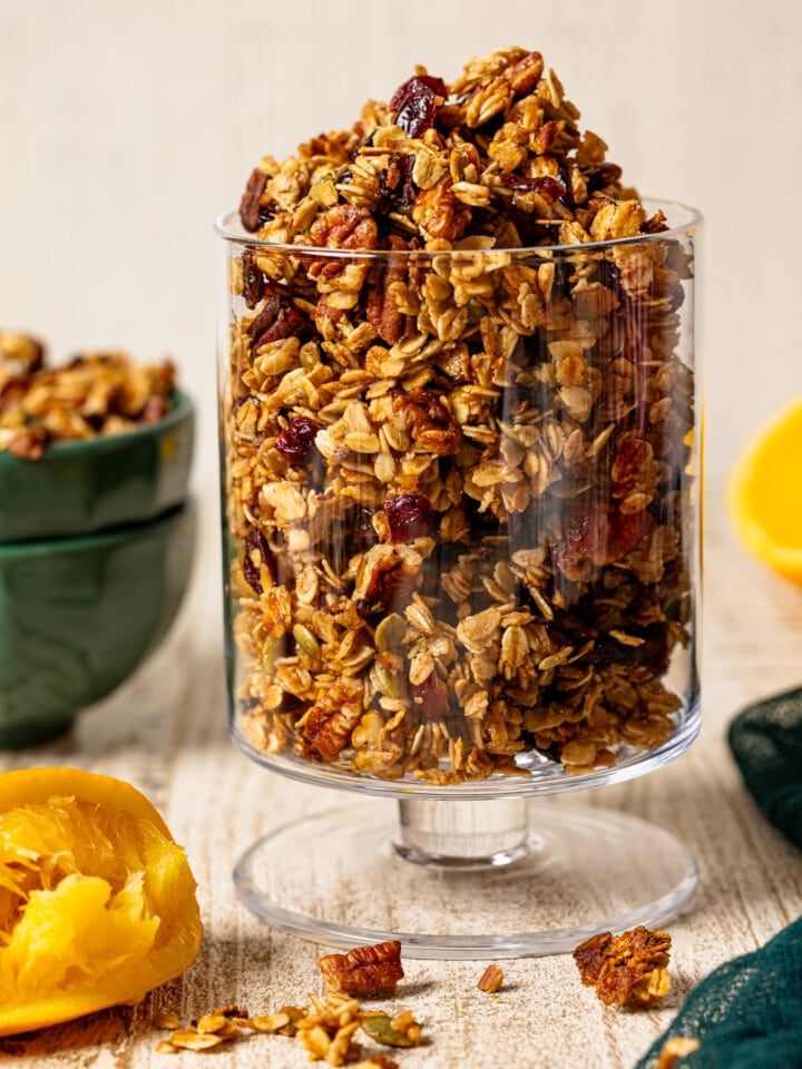 Granola in a trifle bowl with green napkin and oranges.