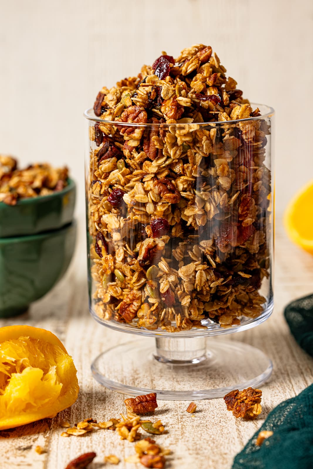 Granola in a trifle bowl with green napkin and oranges.