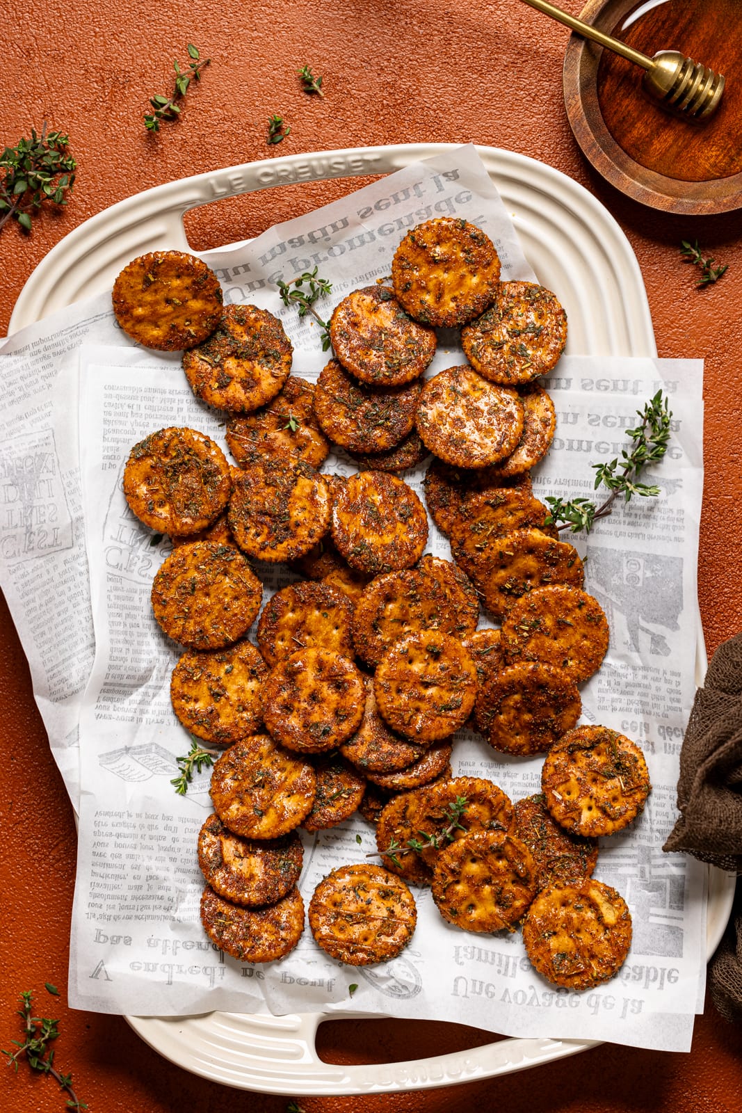 Crackers on a platter with honey on a burnt orange table.