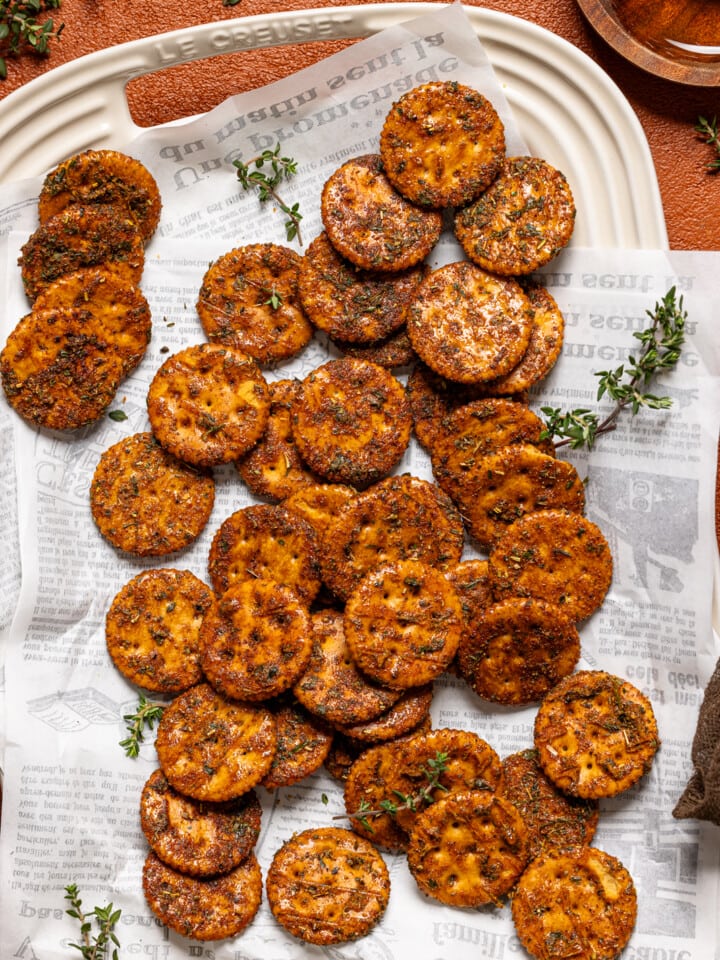 Crackers on a platter with honey on a burnt orange table.